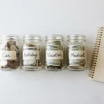 What is a sinking fund 2026 — labeled glass jars on a white shelf each showing a different savings category: car, holiday, vacation, medical